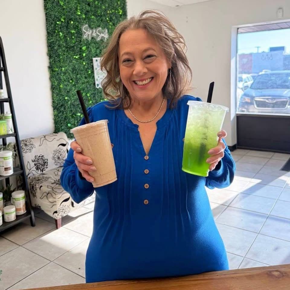 A smiling guest at the counter holding a protein shake and a bright green loaded tea