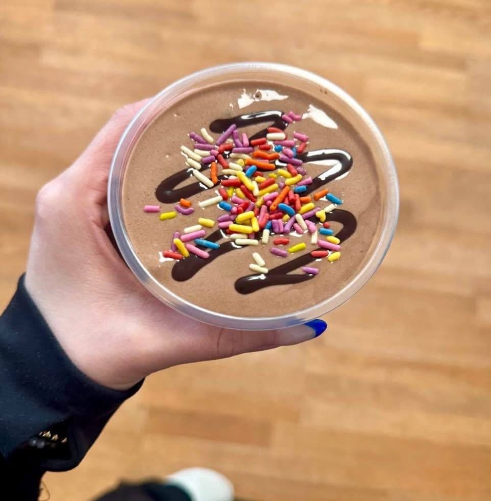 A chocolate protein shake topped with fudge drizzle and rainbow sprinkles